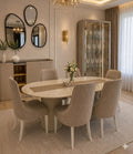 A luxury dining room set featuring a round white marble-top dining table with a ribbed pedestal base, surrounded by six tufted beige velvet chairs. The set is styled in a high-end, elegant dining room with a matching sideboard, wall mirrors, and a glass display cabinet.