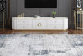A modern white TV console with gold accents and a marble-look top, styled in a contemporary living room setting with a blue-gray rug, dark gray wall, and wooden floor.