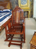 A dark reddish-brown wooden rocking chair with carved details on the backrest, shown in a furniture showroom setting.