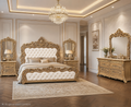 An ornate bedroom set in a luxurious room, featuring a large bed with a tufted cream headboard and matching footboard, flanked by matching gold-framed nightstands and mirrors, with a matching gold-framed dresser on a patterned rug.
